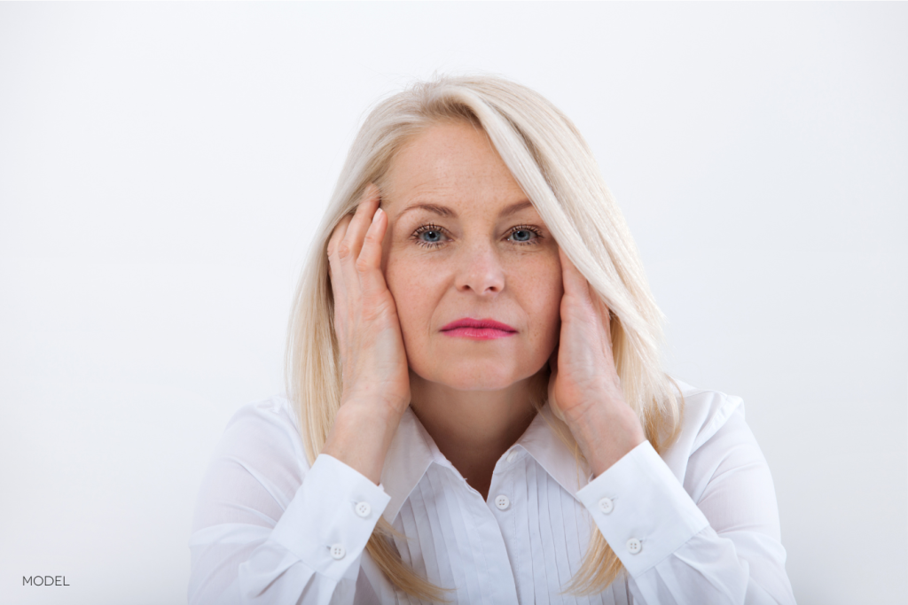 middle aged woman holding her head in her hands and looking at the camera